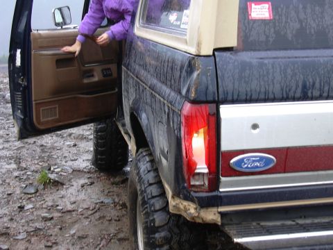1991 Ford Bronco - A person exits a dark blue Ford Bronco with a tan top on a wet, muddy surface.