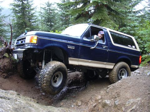 1991 Ford Bronco - A blue Ford Bronco tackles a challenging off-road course with a driver visible inside.