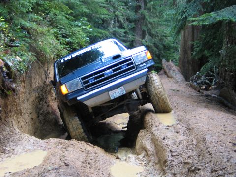 1991 Ford Bronco - This Ford Bronco is tackling a challenging, muddy off-road path in a forest.