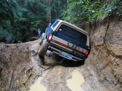 1991 Ford Bronco - A Ford Bronco navigates a challenging muddy terrain, with one side significantly lower than the other.