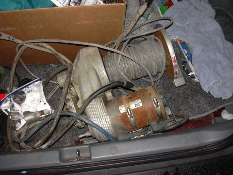 1991 Ford Bronco - Winch and cable are stored in the trunk of a vehicle, alongside other items.