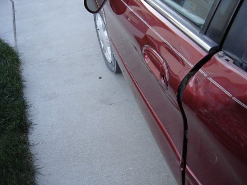 1998 Mercury Sable - The side of a red 1998 Mercury Sable sedan shows damage to the door seam and scratches.