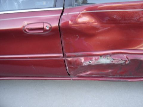 1998 Mercury Sable - Side view of a red car door showing extensive damage, including a large dent and rust, indicating a severe impact.