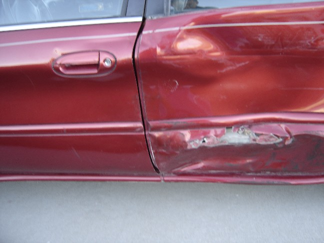 Red car door with heavy damage and rust near the bottom