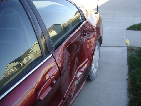 1998 Mercury Sable - The rear passenger side of a red sedan shows extensive damage, including a dented door and missing trim.