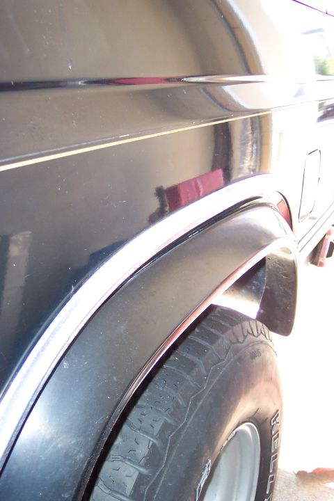 1986 Ford Bronco - The rear quarter panel and tire of a dark SUV are visible, with a thin chrome accent strip.