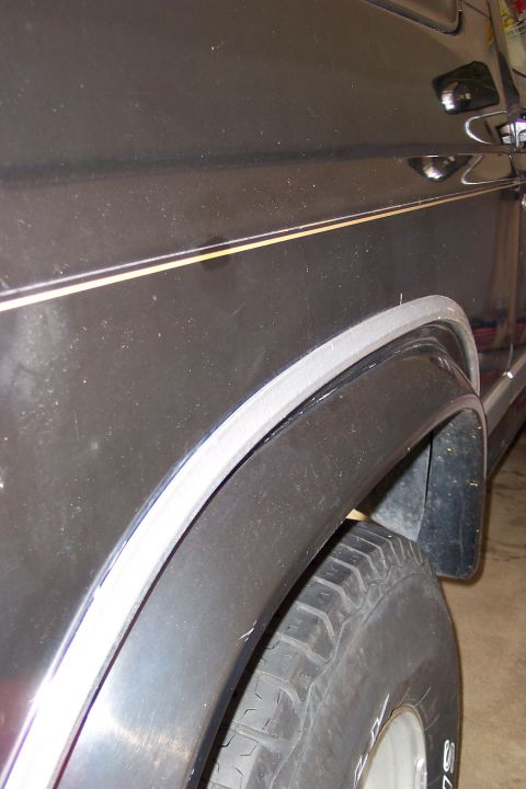 1986 Ford Bronco - The rear quarter panel of a dark SUV shows a distinct body line and fender flare, indicative of an 80s model.