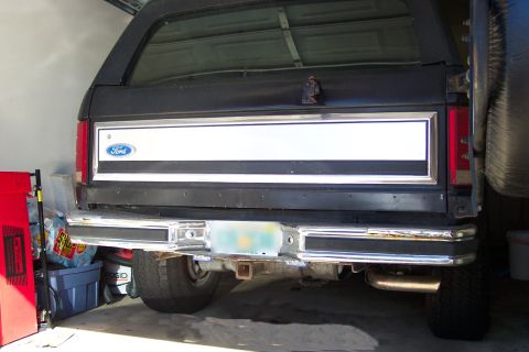 1986 Ford Bronco - The rear of a black 1986 Ford Bronco is visible, showing its tailgate with a white stripe and chrome bumper.