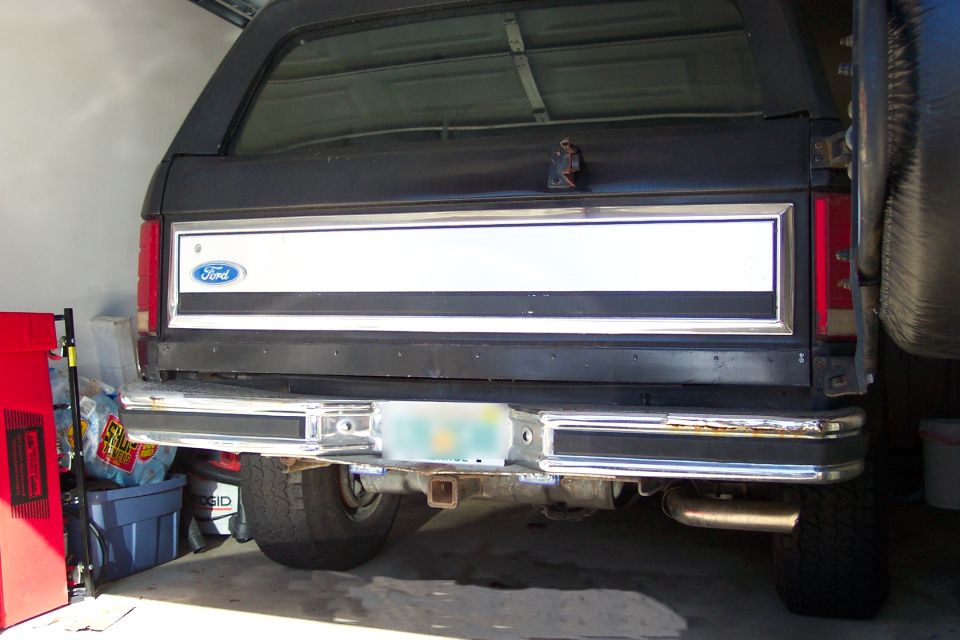 Rear of black 1980s Ford SUV in garage with Ford oval tailgate panel and chrome bumper