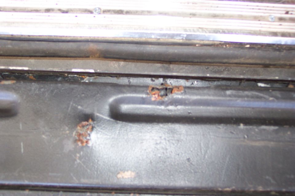Close-up of bubbling rust breaking through paint on a black stamped inner body panel