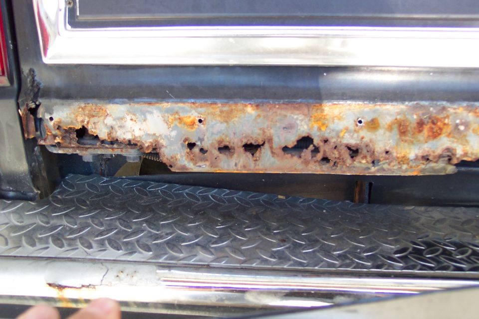 Rust holes through lower rear panel above a diamond-plate rear bumper