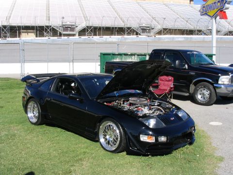1995 Ford Taurus - A black sports car and a black pickup truck are parked on grass with stadium bleachers in the background.