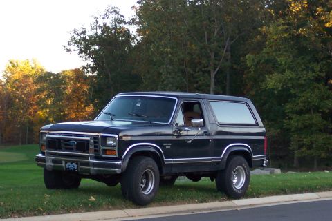 1986 Ford Bronco - This 1986 Ford Bronco is seen from a three-quarter front view, parked on a grassy area next to a road.