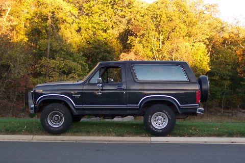 1986 Ford Bronco - This Ford Bronco, likely from the early 1980s, is parked by the side of the road with trees in the background.