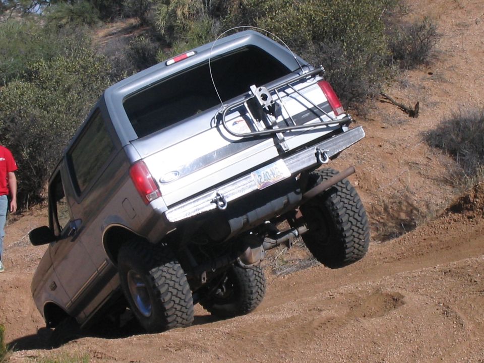 Lifted silver Ford Bronco climbing a steep dirt embankment, rear three-quarter view