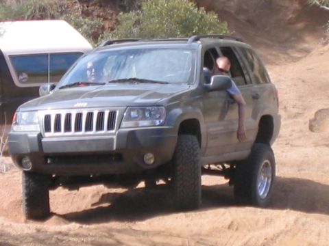 1995 Ford Bronco - A lifted Jeep Grand Cherokee navigates a dirt trail, with another vehicle partially visible in the background.