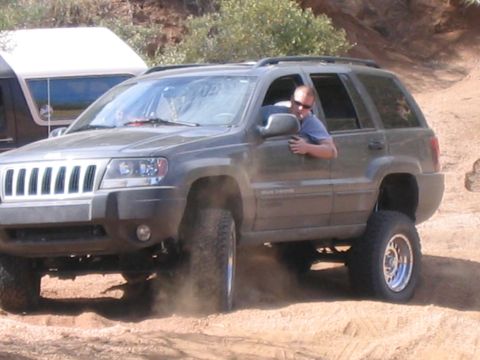 1995 Ford Bronco - A dark green SUV navigates a dusty off-road trail, its lifted suspension and aggressive tires. Another vehicle is partially visible in the…