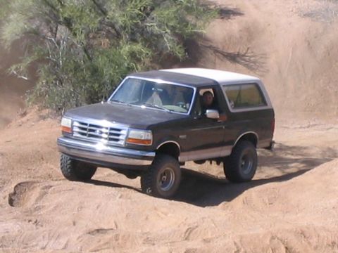 1995 Ford Bronco - A person drives a Ford Bronco through a sandy, off-road trail with sparse vegetation.