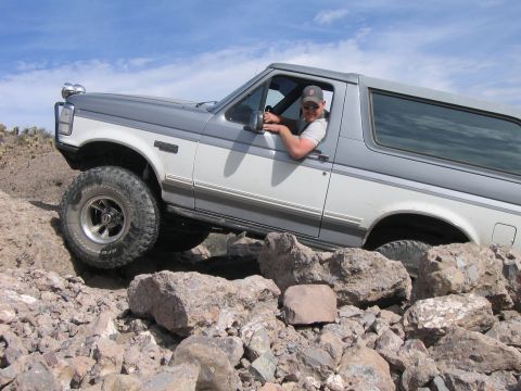 1995 Ford Bronco - A driver maneuvers a two-tone Ford Bronco through a challenging rocky off-road course.