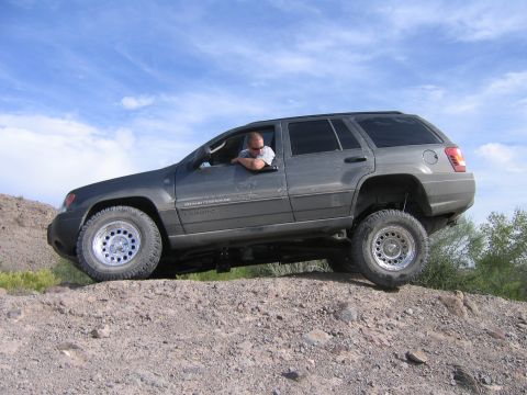 1995 Ford Bronco - Driver navigates a Jeep Grand Cherokee over rough terrain under a blue sky.