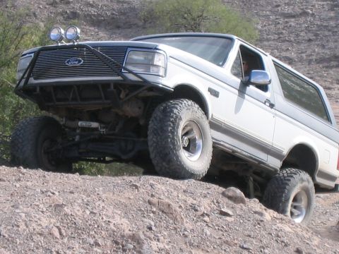1995 Ford Bronco - Modified white Ford Bronco navigates a steep, rocky incline.
