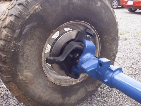 1988 Ford Bronco - Front axle assembly with tire and brake rotor, with other vehicles in the background.