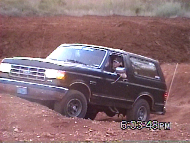 Black Ford Bronco driving on a dirt hill. Driver visible