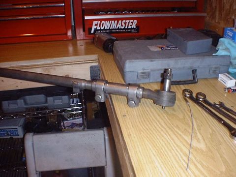 1988 Ford Bronco - Steering linkage part with tie rod end, on a wooden surface next to tools and a toolbox.