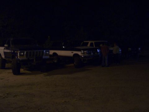 1996 Ford Bronco - Several vehicles are parked outside at night, illuminated by artificial light.
