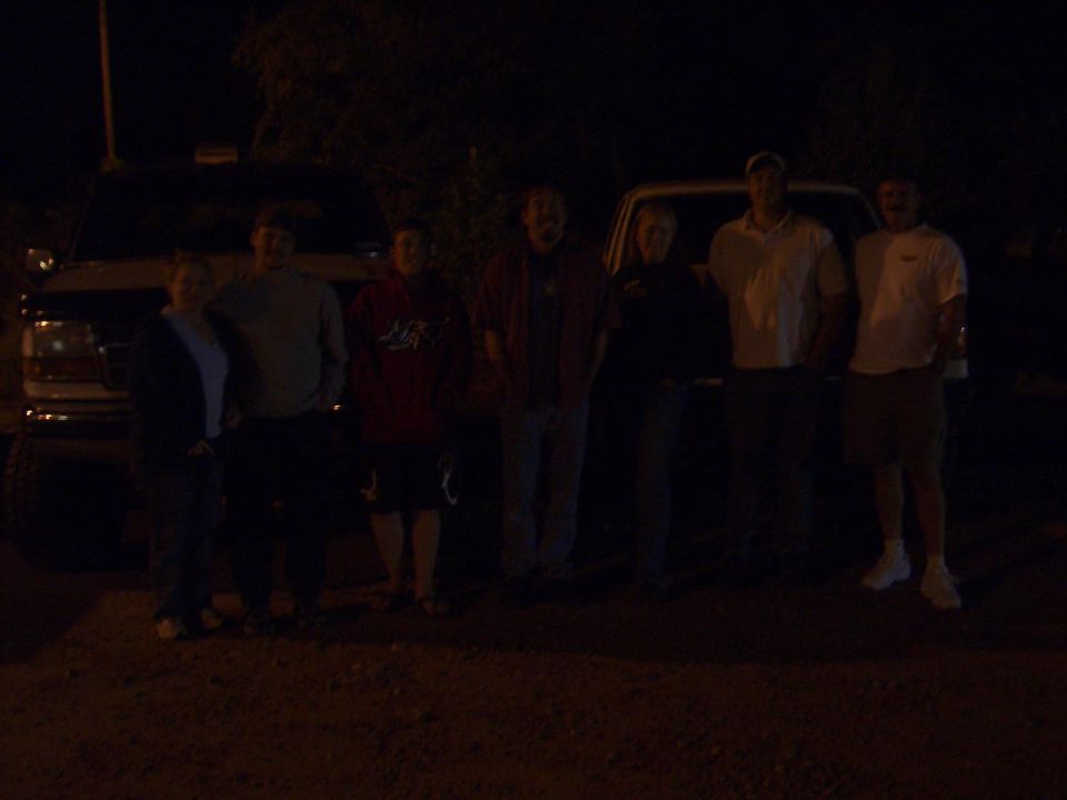 Group of people posing at night in front of light-colored trucks on gravel