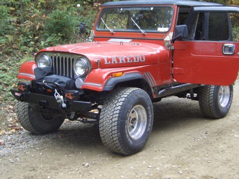 1996 Ford Bronco - A red Jeep CJ-7 Laredo is parked on a dirt road with its driver's door open.