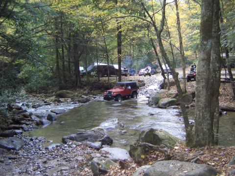 1996 Ford Bronco - Several off-road vehicles are seen navigating a rocky stream in a forest during autumn.