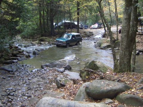 1996 Ford Bronco - Green 1996 Ford Bronco navigates a rocky stream bed surrounded by trees.