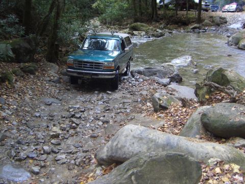1996 Ford Bronco - Ford Bronco driving through a rocky stream in a wooded area.