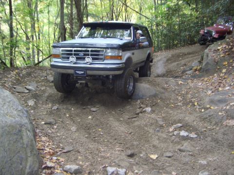 1996 Ford Bronco - A Ford Bronco drives off-road with another vehicle visible behind it on a steep, dirt path.