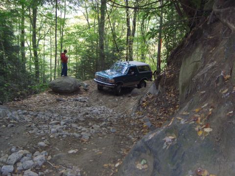 1996 Ford Bronco - Ford Bronco driving off-road on a steep, rocky path surrounded by trees.