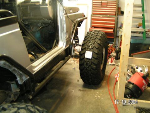 1978 Ford Bronco - A large off-road tire is positioned next to the open door of a vehicle, revealing its interior roll cage and wiring.