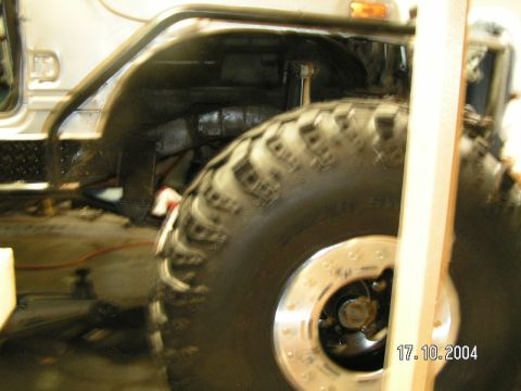 1978 Ford Bronco - A close view of a vehicle's tire and wheel well, with a wooden post obscuring part of the image.