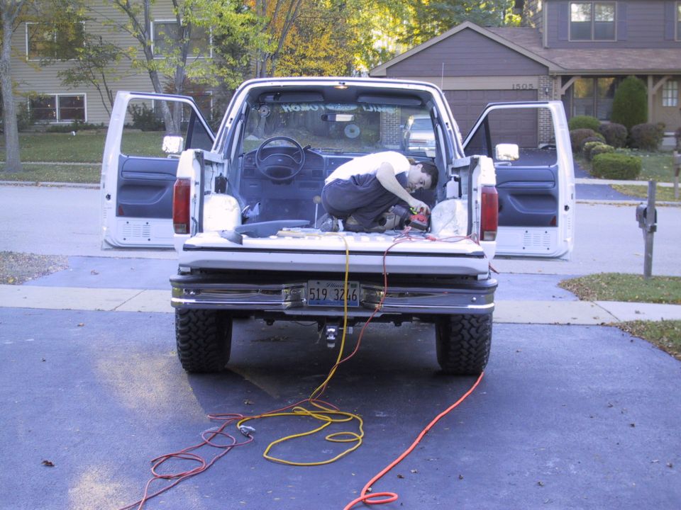 Guy working on the inside of a white Ford truck bed, doors open. Power cords run from the back