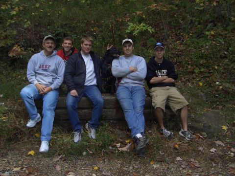 1996 Ford Bronco - A group of five men and a dog are gathered outdoors, sitting on a log in a natural setting.
