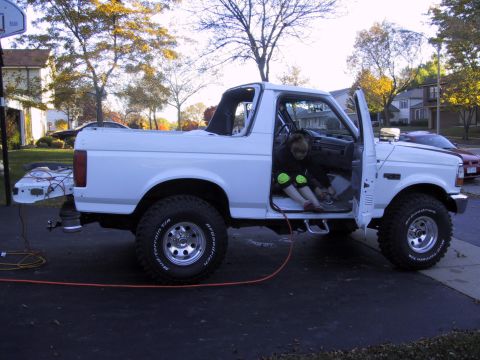 1993 Ford Bronco - White 1992 Ford Bronco with driver's door open, child sitting inside. Rear bumper removed.