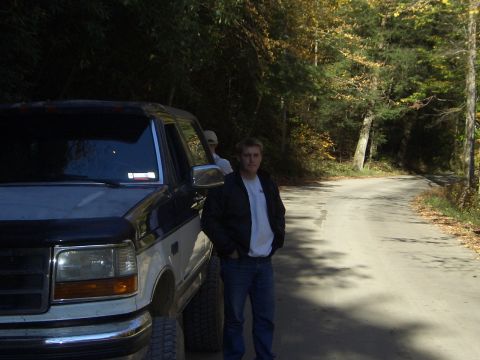 1996 Ford Bronco - Man stands next to a two-tone Ford F-Series truck on a tree-lined road.