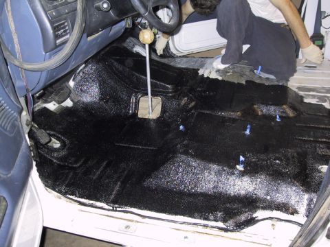 1993 Ford Bronco - The interior floor of a vehicle is being treated with a black protective coating, with a person visible working on it.