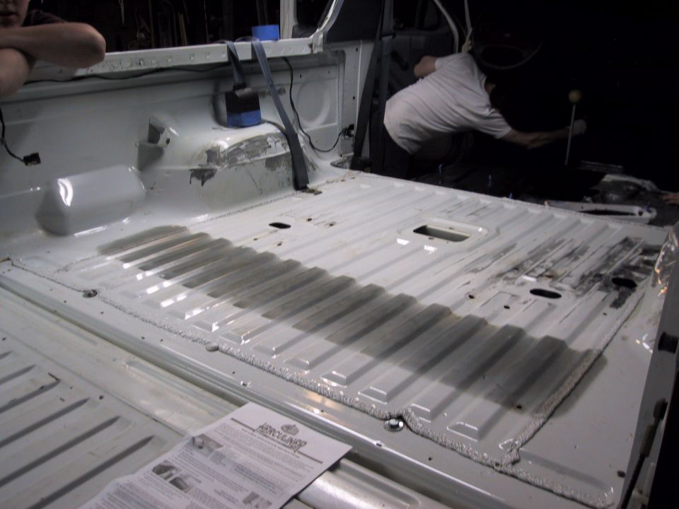 Interior of a white truck bed with a person working on the floor. There's a Herculiner instruction sheet on the floor