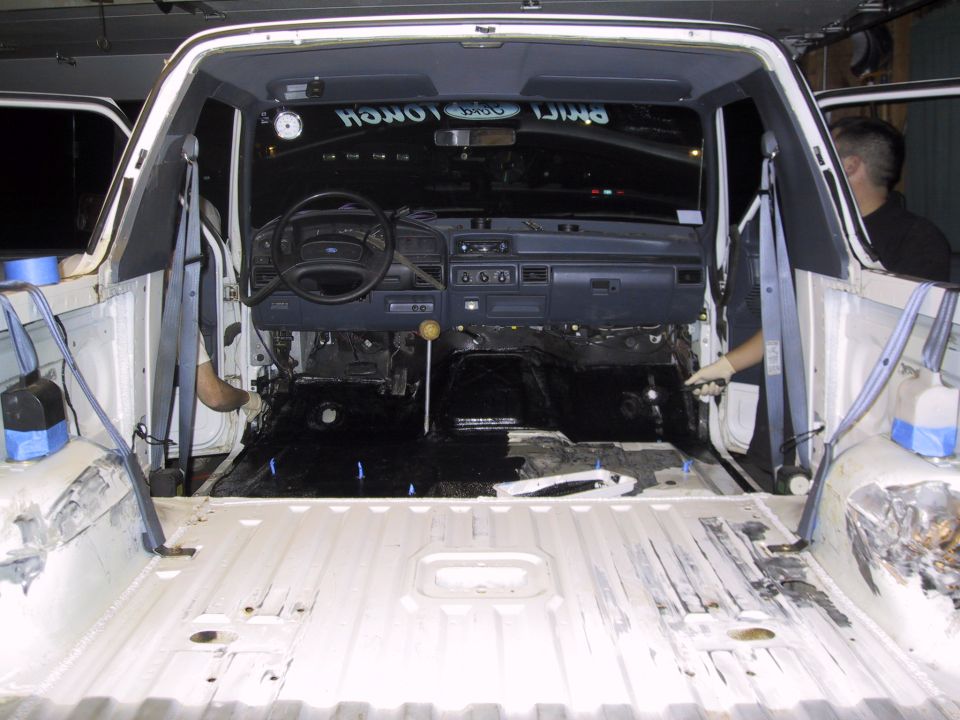 1993 Ford Bronco interior stripped down, showing dashboard, steering wheel, and empty floor. White body panels are visible