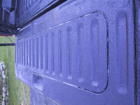 1993 Ford Bronco - Close-up of a purple truck bed liner a ribbed texture and a recessed area.