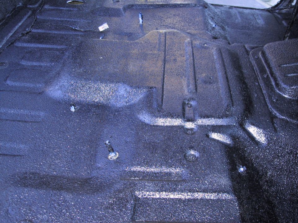 vehicle floor with spray-on bedliner, showing some bolts and a white tag