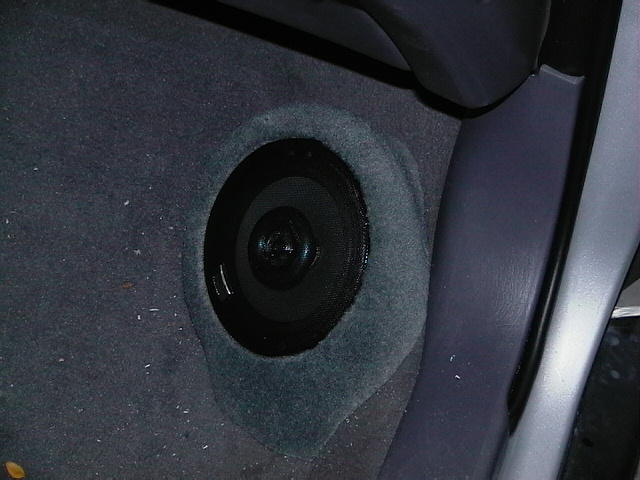 Car interior shot showing a round speaker installed in the carpeted floor near the seat