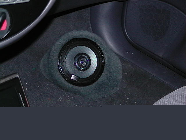 Car interior shot showing a speaker mounted in the carpeted floor area near the dashboard