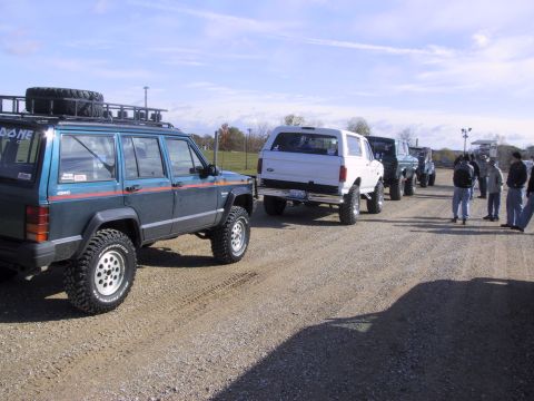 1993 Ford Bronco - A line of SUVs and trucks are parked on a gravel lot under a partly cloudy sky.